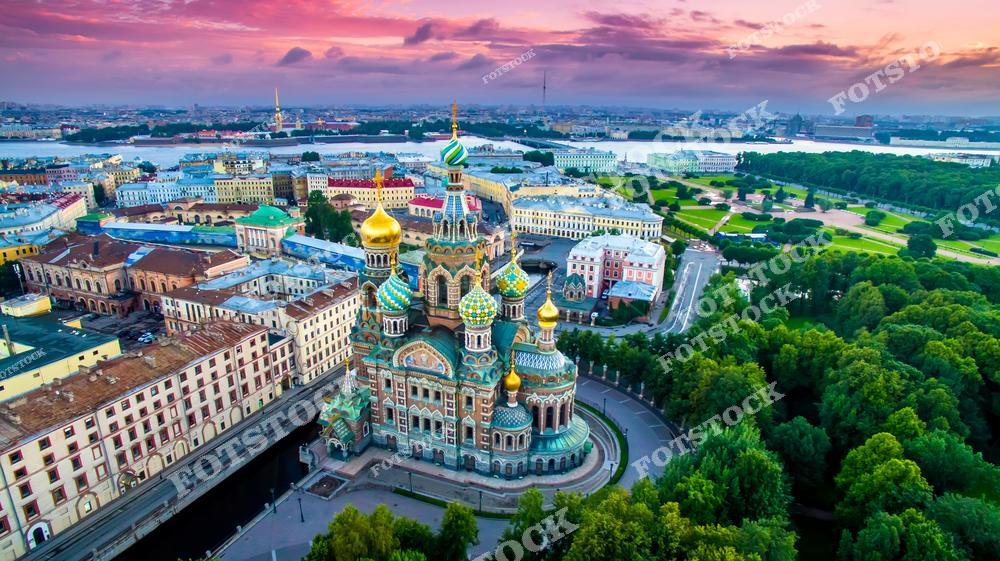 Фотография панорамного вида Санкт-Петербург, Россия, сделанная летом на закате. На изображении запечатлён Храм Спаса на Крови, также известный как Собор Воскресения Христова, на фоне тёплого вечернего неба. Фотоснимок передаёт атмосферу летнего заката, подчёркивая выразительную архитектуру храма и силуэты исторического центра города. Фото отражает культурное наследие Петербурга, его музеи и архитектурные памятники, формируя образ одного из самых узнаваемых городов России. Иллюстрация может использоваться как фото, картинка или слайд, посвящённые архитектуре и городским панорамам Российской Федерации.